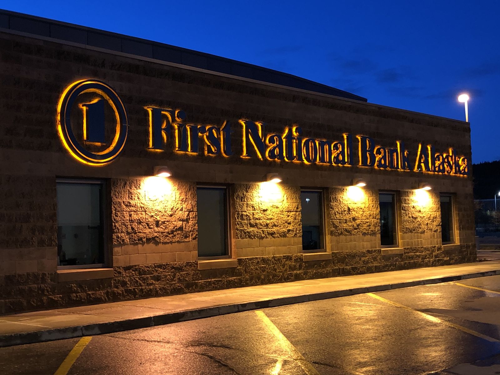 A bank's stone frontage and sidewalk at night, the pavement still wet from washing