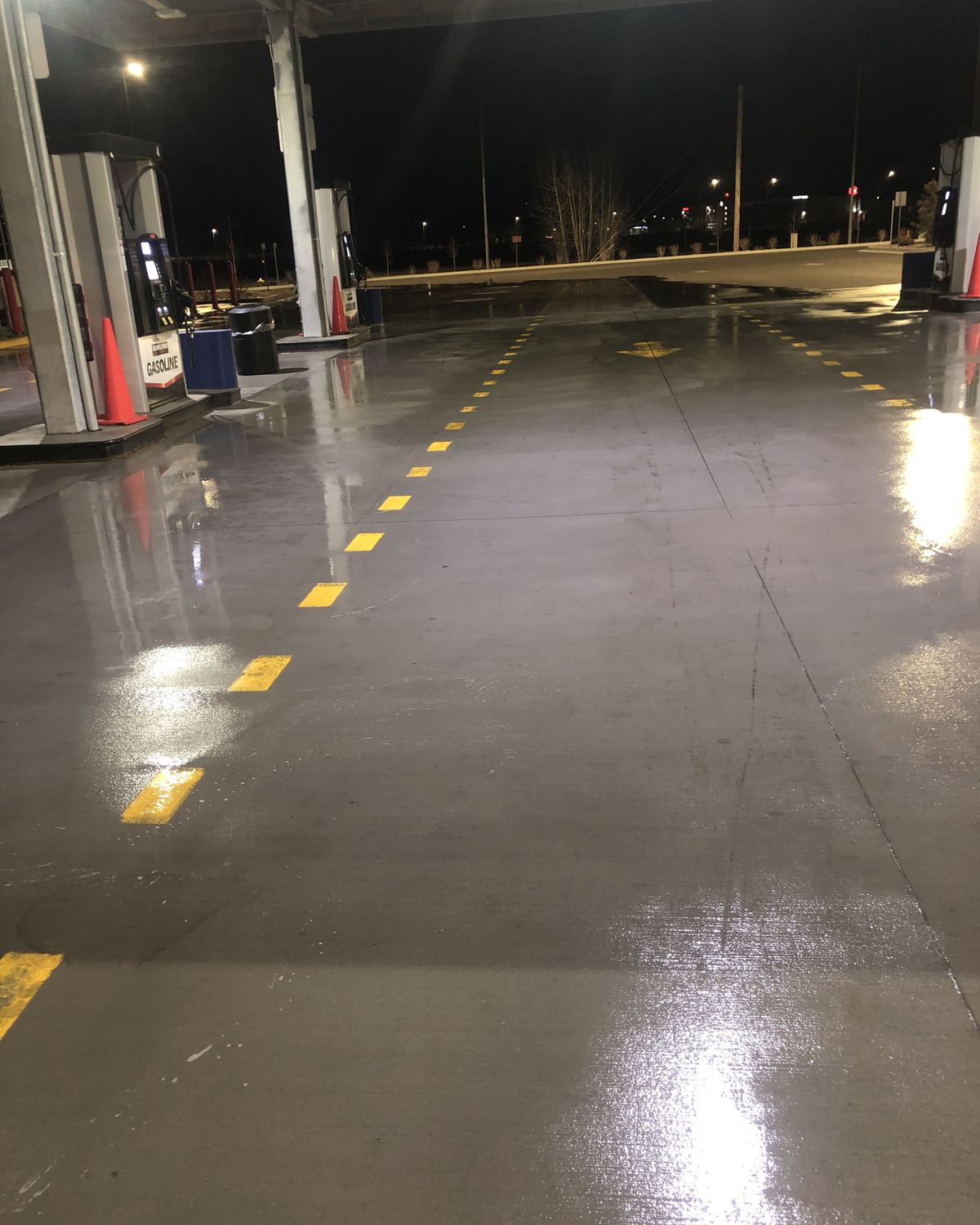 A fuel station pad under its canopy at night, the concrete washed and shining under the lights