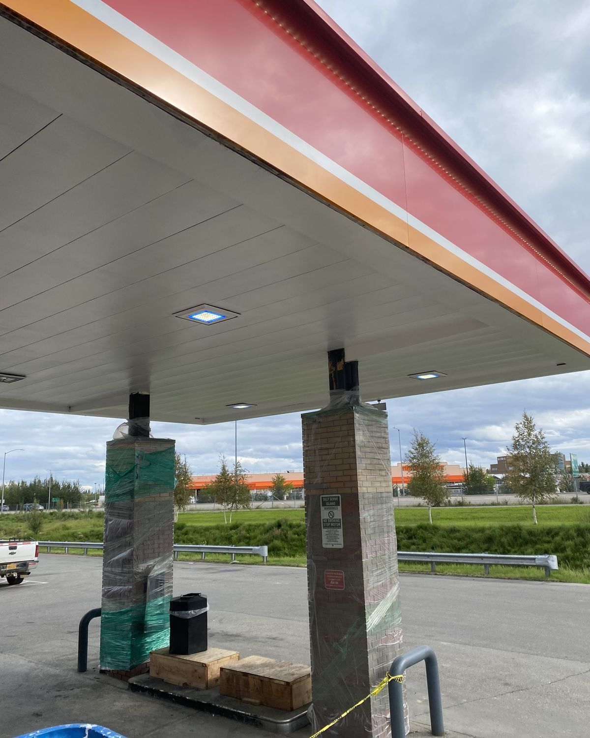 The same fuel station canopy with its ceiling panels back to white, two columns still wrapped for repair