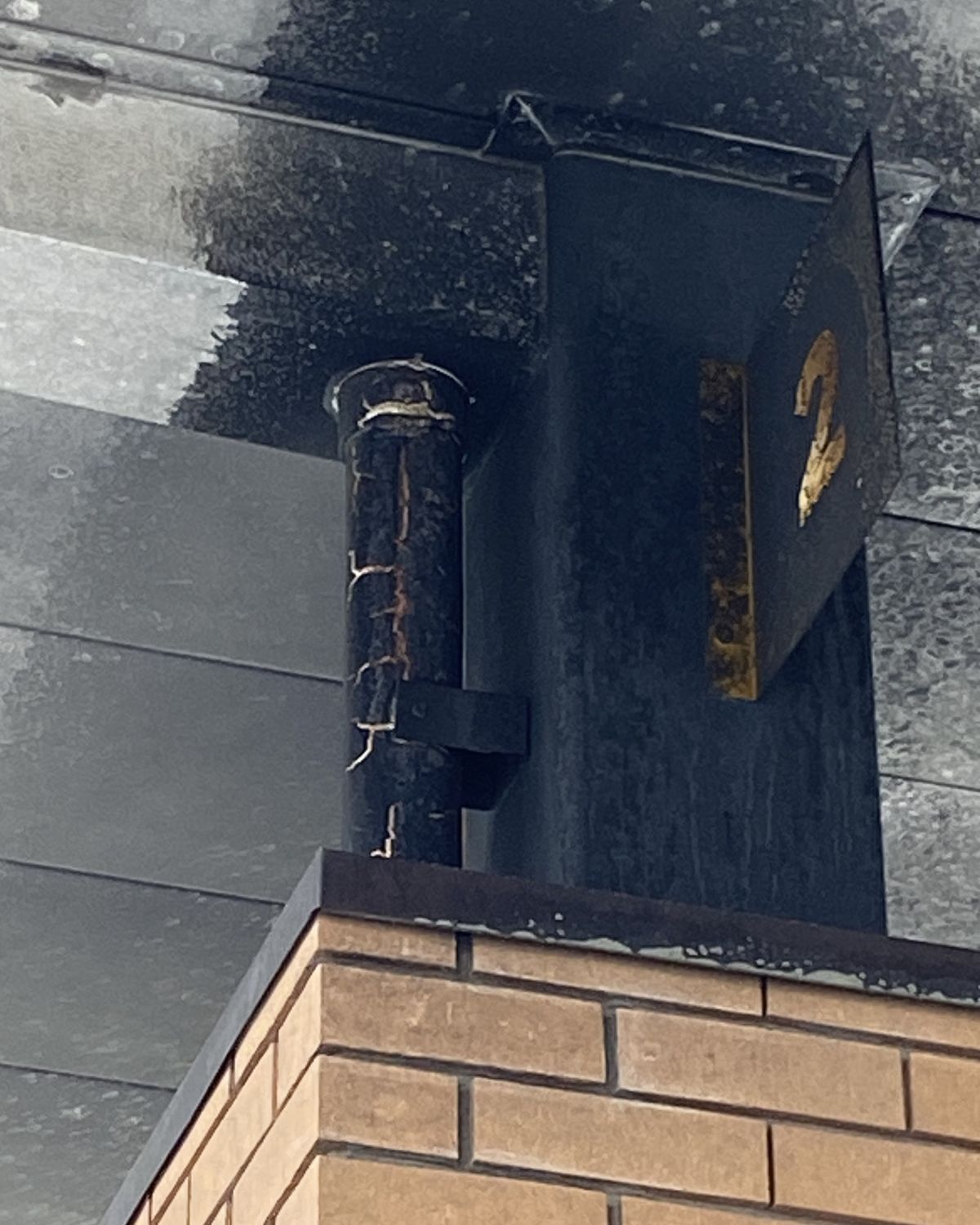 A canopy support and pump number sign blackened with soot above a brick column