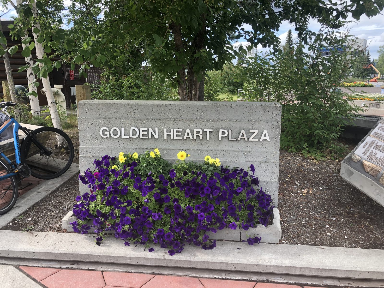 The Golden Heart Plaza sign in downtown Fairbanks, a planter of purple and yellow petunias in front of it