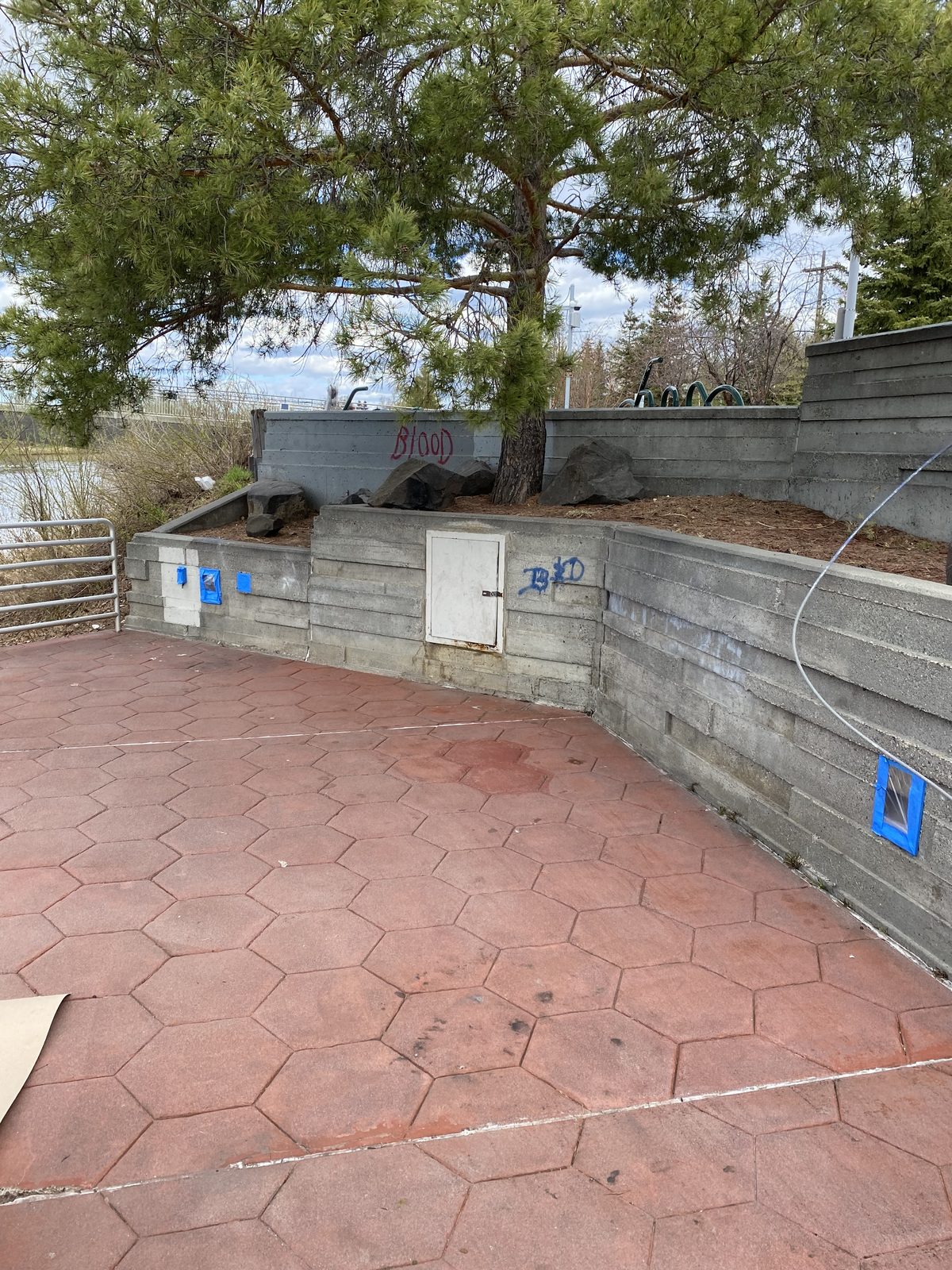 The plaza's board-formed concrete walls taped off for paint, tags still visible on the back wall