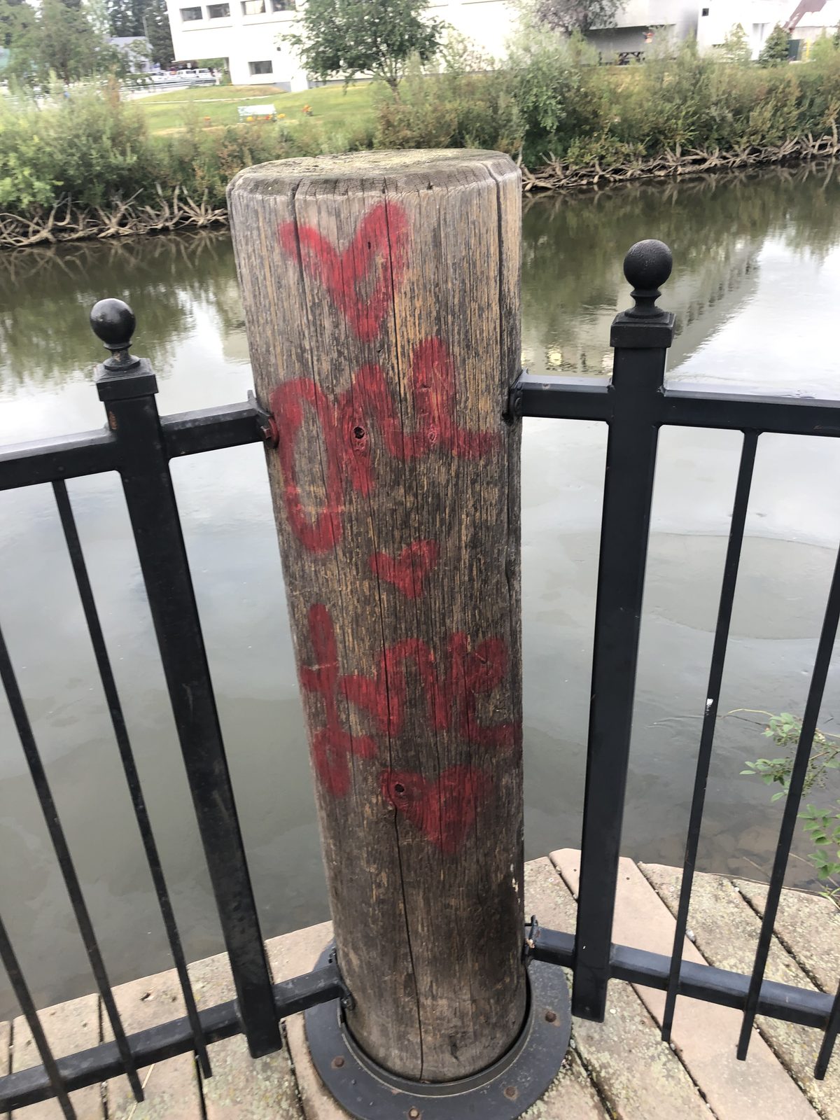 A wooden post on the river walk covered in red spray paint, the railing and river behind it