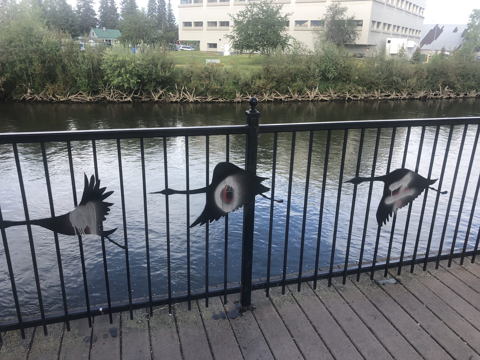 The river walk railing above the water, its steel crane cut-outs sprayed with tags