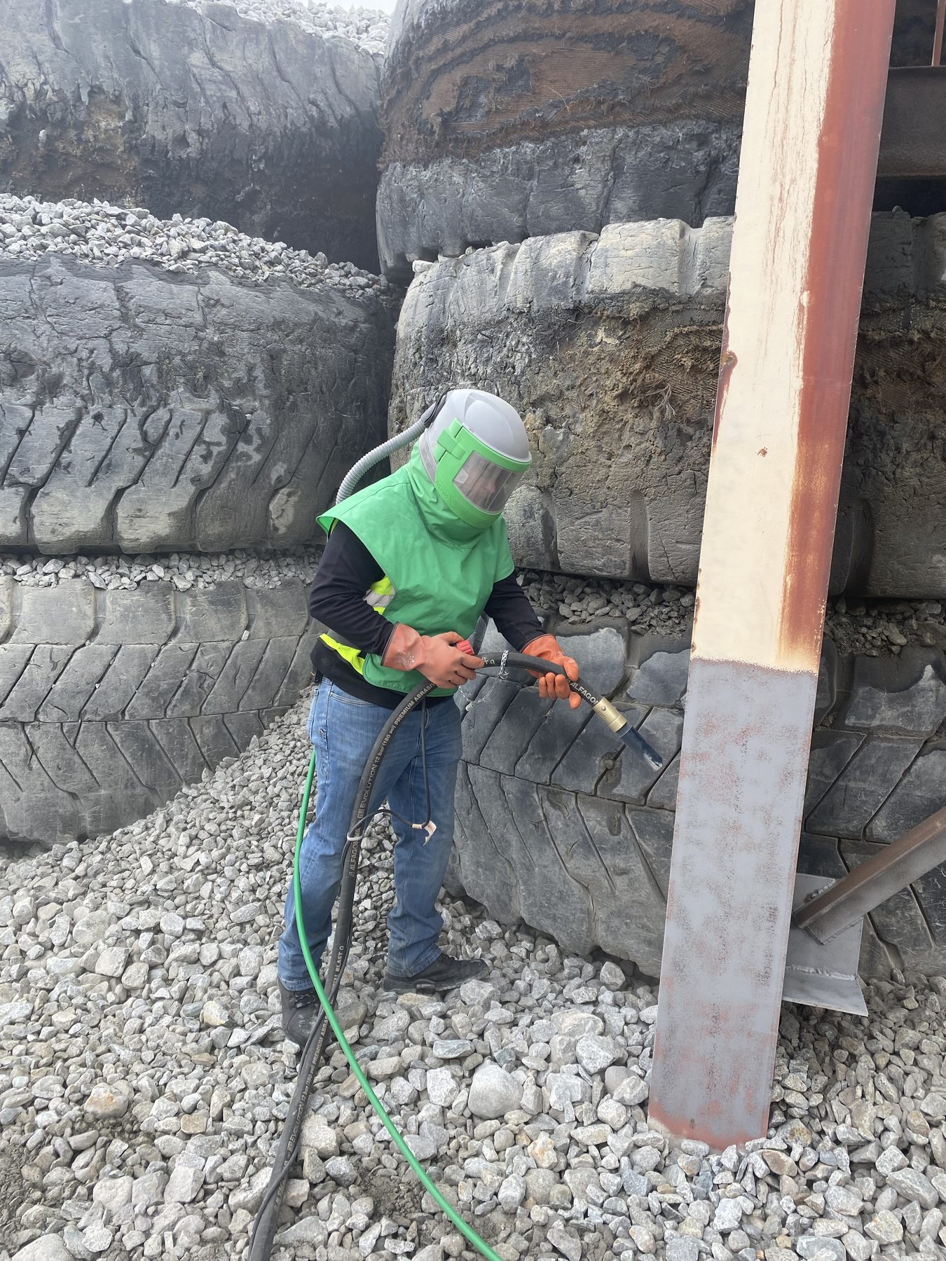 Blasting a structural steel column, the lower half already back to bare metal