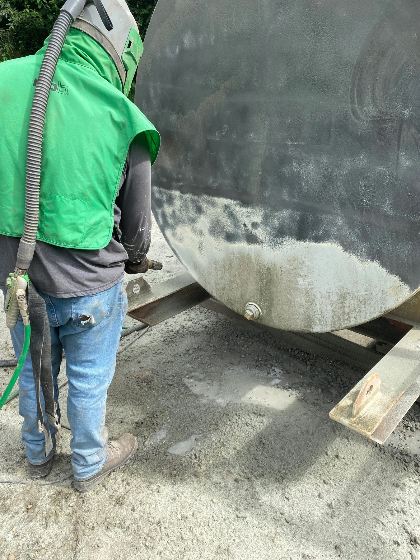 Blasting the side of a steel tank, spent media banked up on the ground