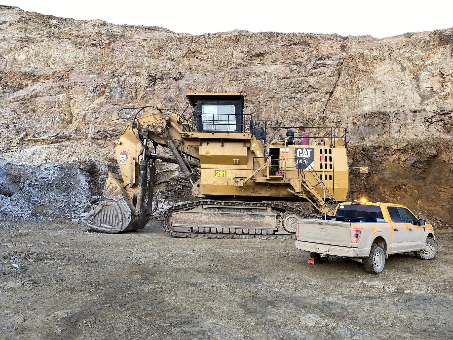 A hydraulic mining shovel in a rock pit, a full-size pickup parked alongside it