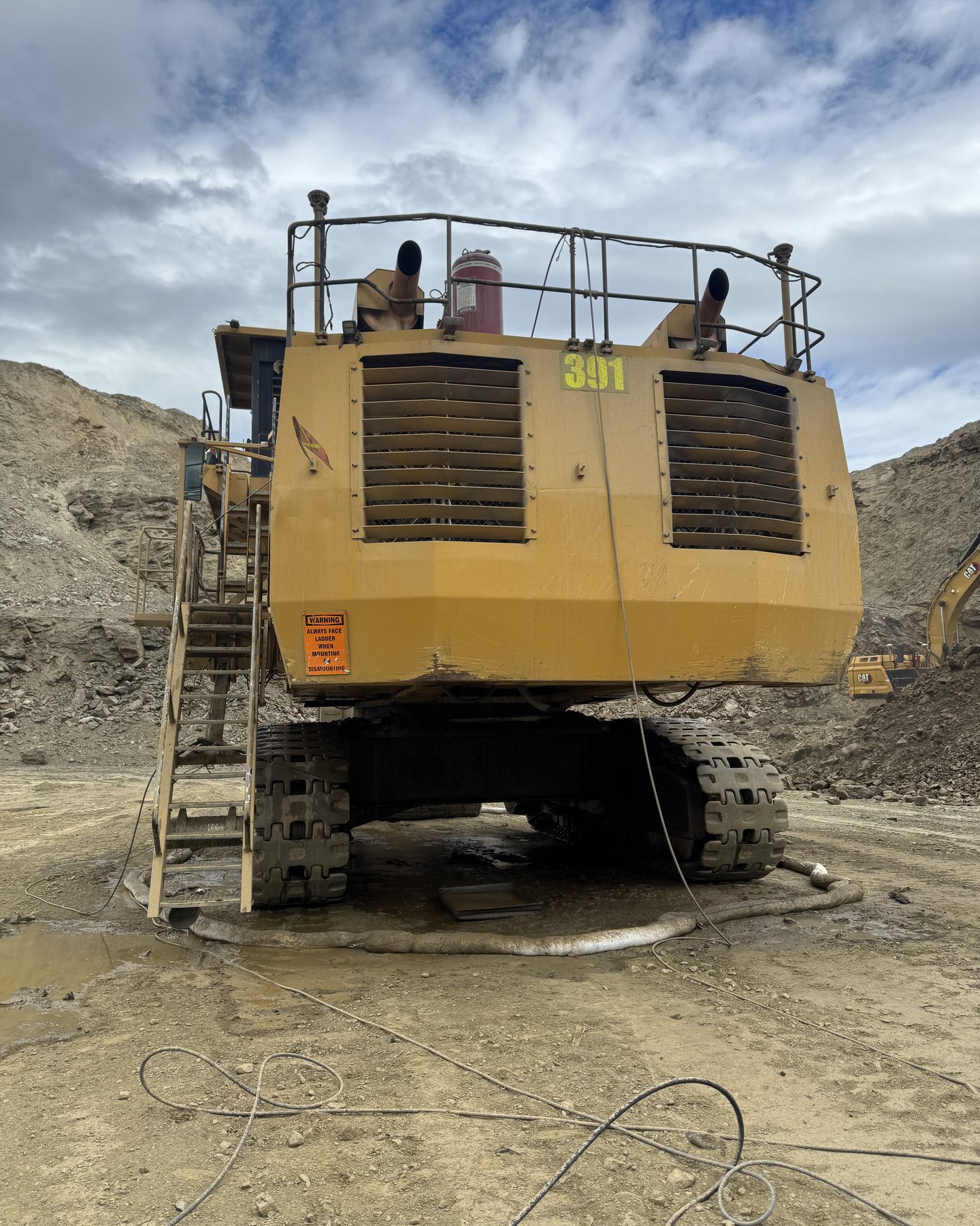 The back of a mining shovel on wet ground, pressure hoses run out across the mud