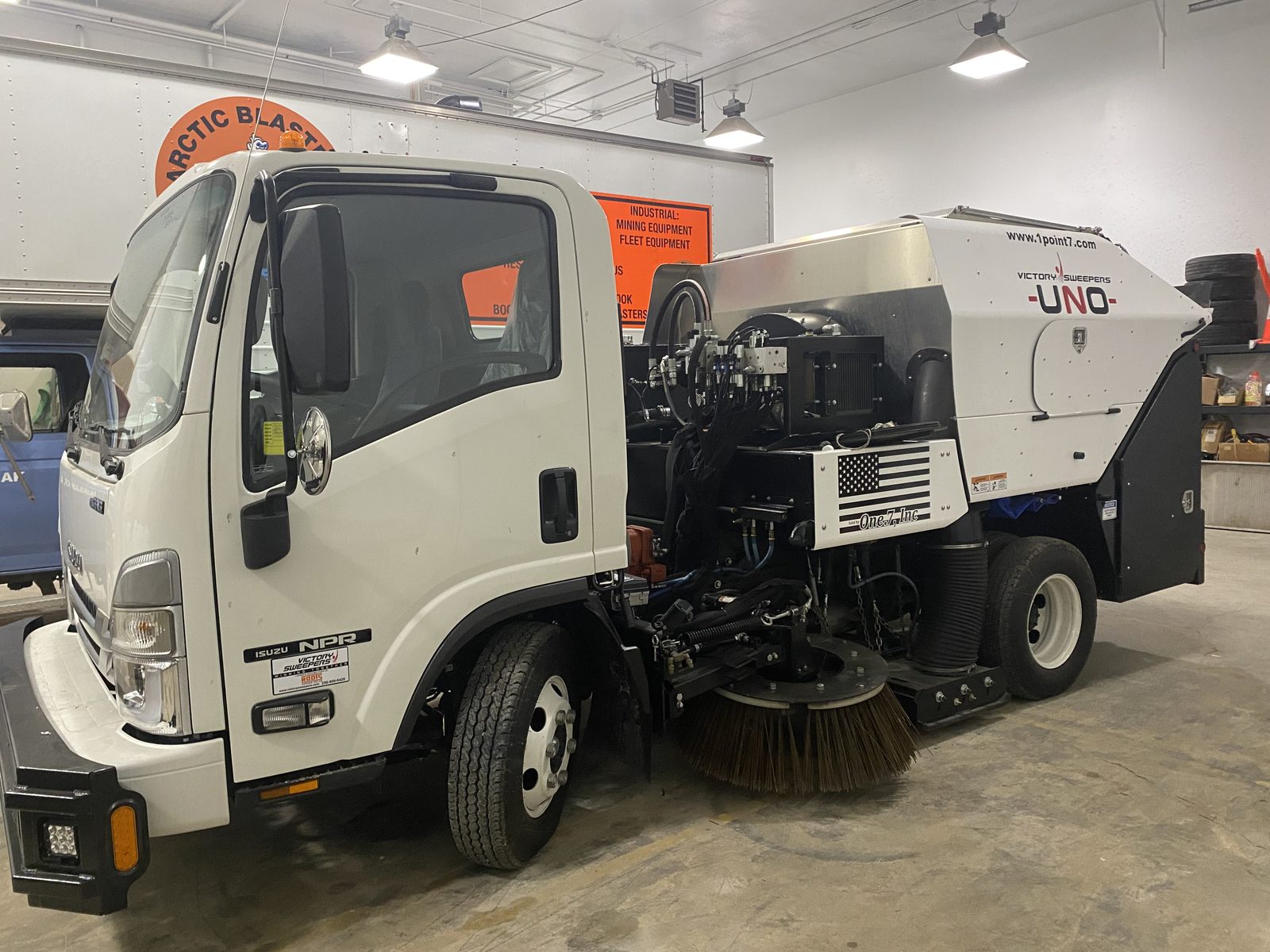 The Arctic Blasters sweeper truck parked in the shop, side brooms down, the company sign on the wall behind it