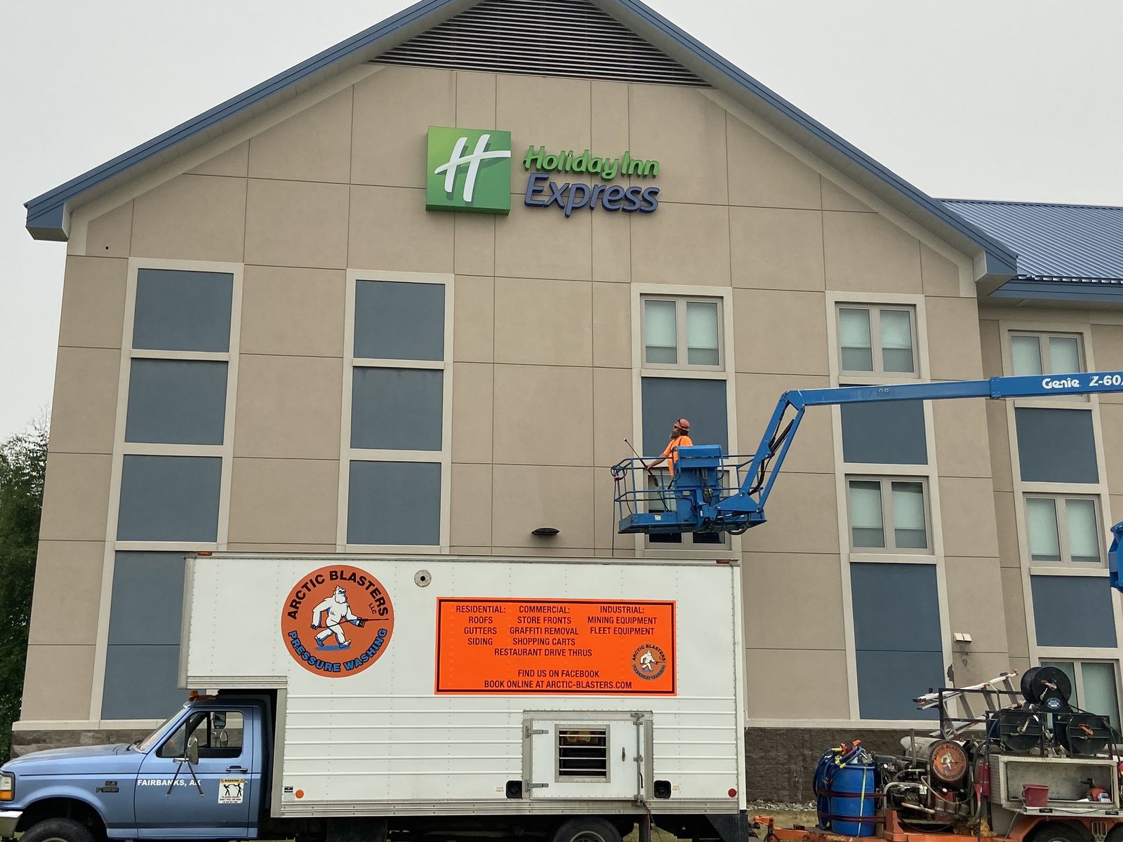 The Arctic Blasters box truck parked in front of a three-storey hotel, Joel up on a boom lift against the wall